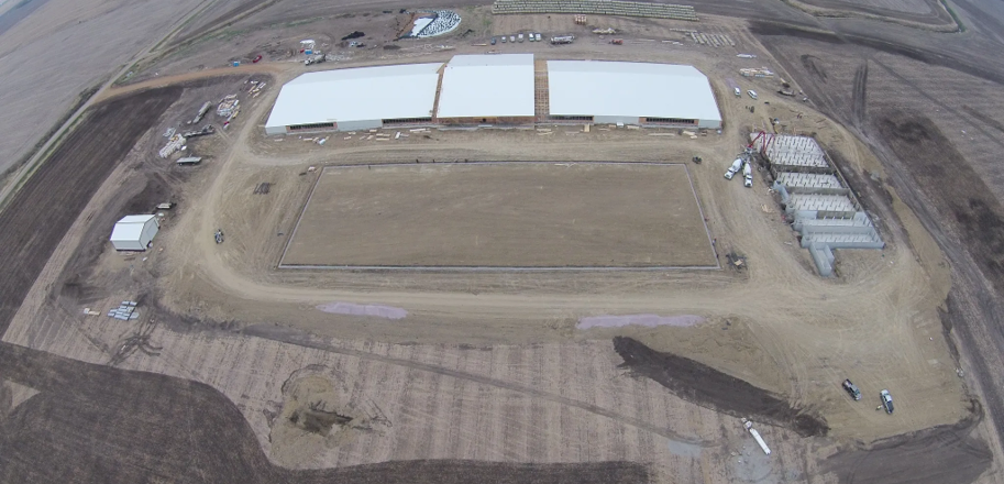 Aerial view of a swine site under construction: buildings framed and roofed, pit poured, slats stacked on site